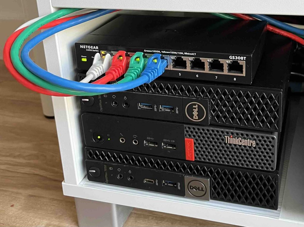 Photo of three mini pc's and a switch above it with ethernet cables attached.